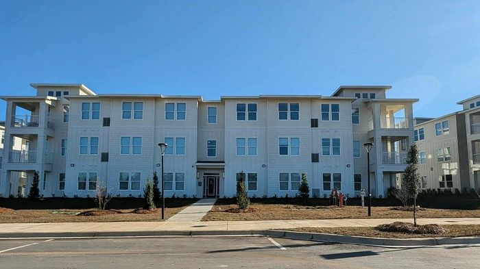 Modern three-story apartment complex with spacious balconies and well-maintained landscaping under a clear blue sky.