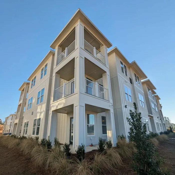 Elegant three-story apartment complex with modern architecture, lush landscaping, and spacious balconies under a clear blue sky.