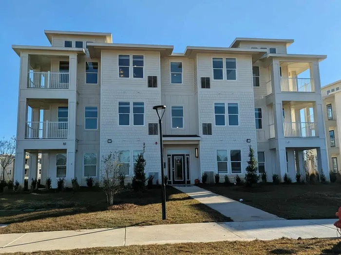 Modern three-story apartment building with spacious balconies and large windows, surrounded by well-kept greenery and a welcoming walkway.