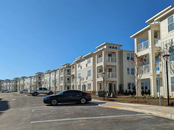 Modern apartment complex showcasing elegant balconies and ample parking under a clear blue sky.