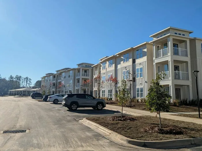 Modern apartment complex with spacious balconies, ample parking, and serene surroundings on a sunny day.