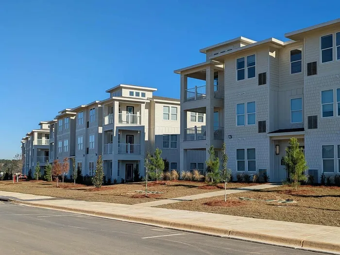 Bright and modern apartment complex with spacious balconies and attractive landscaping under a clear blue sky.