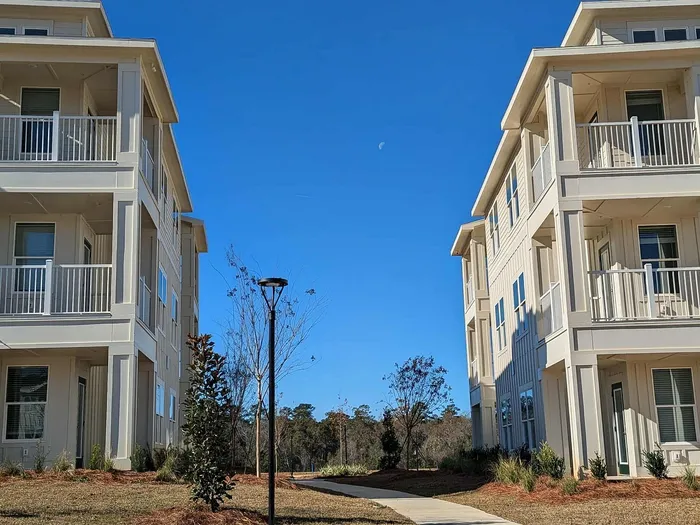 Charming apartment complex with modern three-story buildings, surrounded by lush greenery under a clear blue sky.