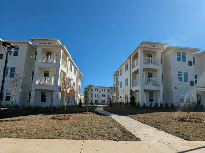Modern apartment complex with elegant three-story buildings featuring private balconies, set against a clear blue sky, offering a serene and stylish living environment.