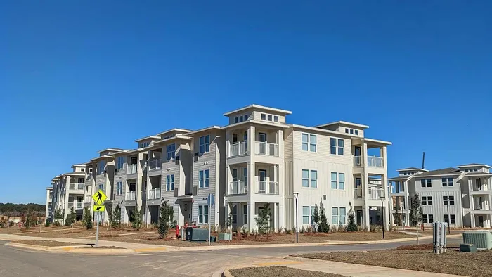 Modern apartment complex with spacious balconies and beautiful landscaping under a clear blue sky.