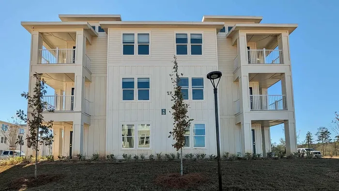 Elegant three-story apartment with modern balconies, large windows, and charming exterior design set against a clear blue sky.