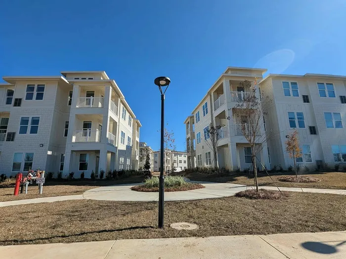 Elegant apartment complex showcasing modern architecture with bright facades, spacious balconies, and lush landscaping under a clear blue sky.