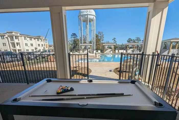 Modern apartment complex with a poolside view featuring a billiards table, luxurious poolside cabanas, and a vibrant outdoor setting.