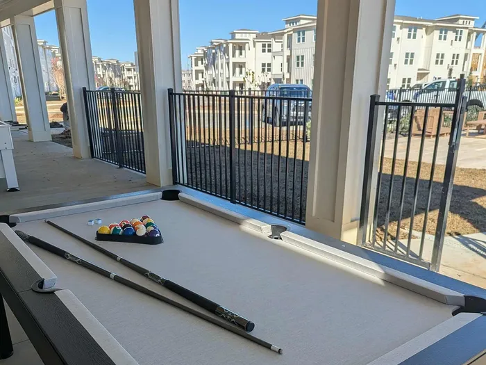 Chic outdoor recreation area with a pool table, perfect for leisure, set against modern apartment buildings under clear blue skies.