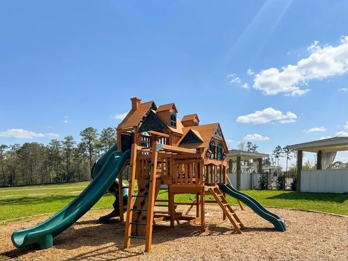 Charming wooden playground with slides and climbing areas set in a sunny, spacious outdoor environment.