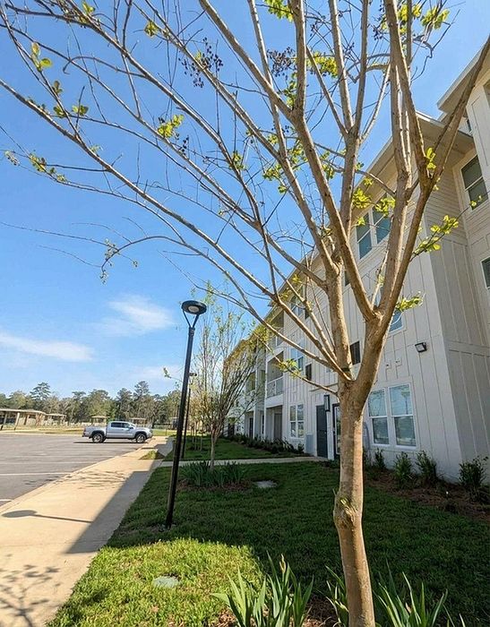 Modern apartment exterior with lush greenery and ample parking in a serene neighborhood setting.