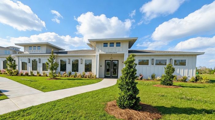 Charming modern house with elegant design, surrounded by lush green lawns and vibrant landscaping under a bright blue sky.