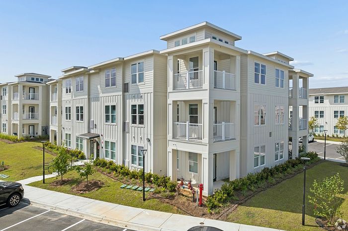 Modern apartment building with elegant white facade, featuring multiple balconies and lush green landscaping.