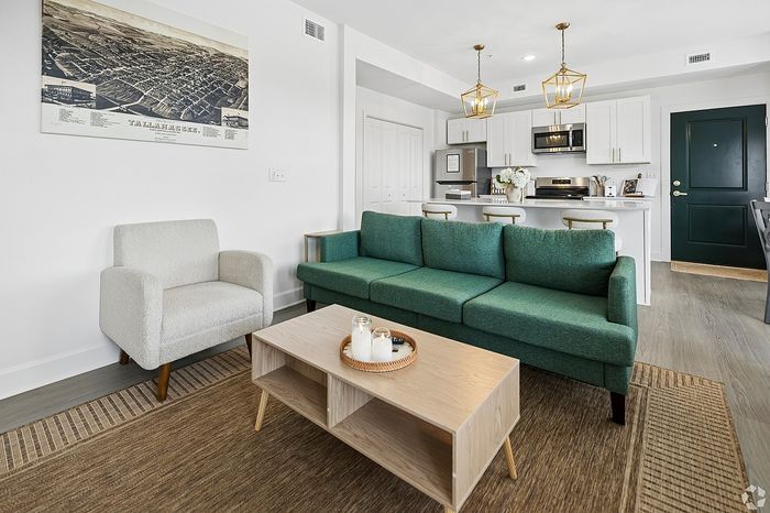 Modern living room with a stylish green sofa, cozy armchair, and chic kitchen island in a bright open-plan apartment.