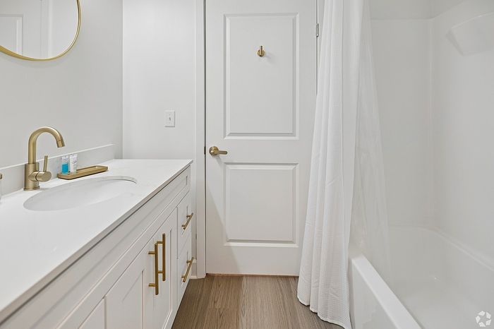 Bright and elegant bathroom featuring a sleek white vanity, luxurious gold fixtures, and a serene bathtub with stylish wood flooring.
