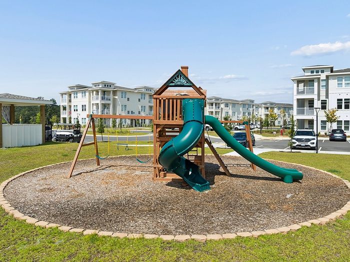 Inviting community playground with modern slide and swings, surrounded by stylish apartment buildings under a clear blue sky.