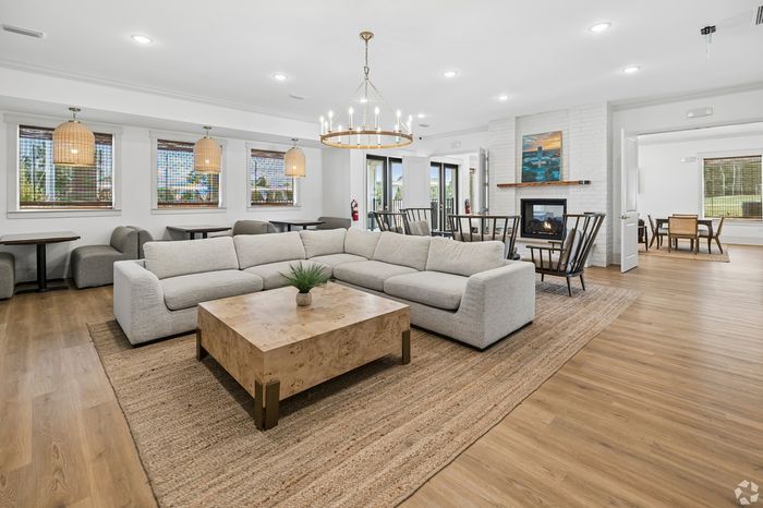 Chic living area with a cozy beige sectional, modern chandelier, and inviting fireplace, featuring elegant hardwood floors and ample natural light.
