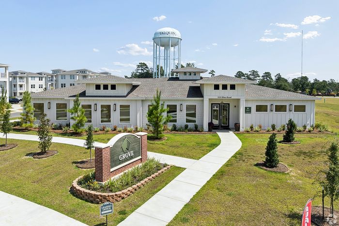 Charming leasing office at The Grove, surrounded by lush landscaping and modern apartment buildings with a scenic watertower backdrop.