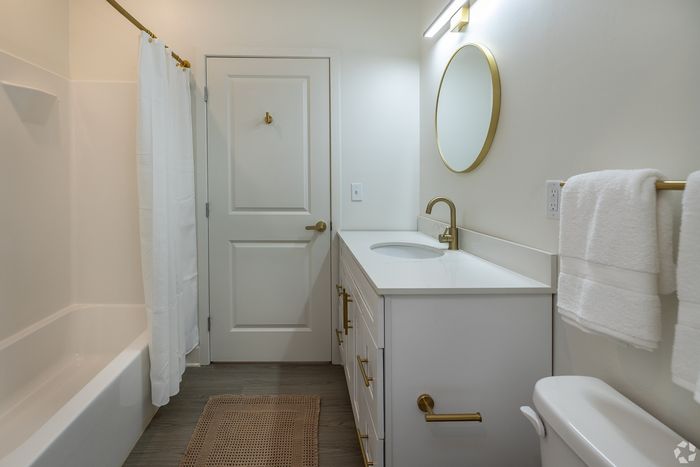Modern bathroom with elegant gold fixtures, round mirror, and pristine white cabinetry.