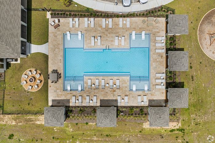 Luxurious apartment outdoor area featuring a sparkling pool with poolside loungers, shaded cabanas, and a stylish fire pit area for relaxation and entertainment.