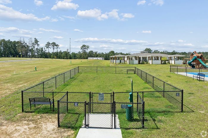 Beautiful dog park with fenced area and benches in a green open space next to modern apartment buildings, perfect for outdoor activities.