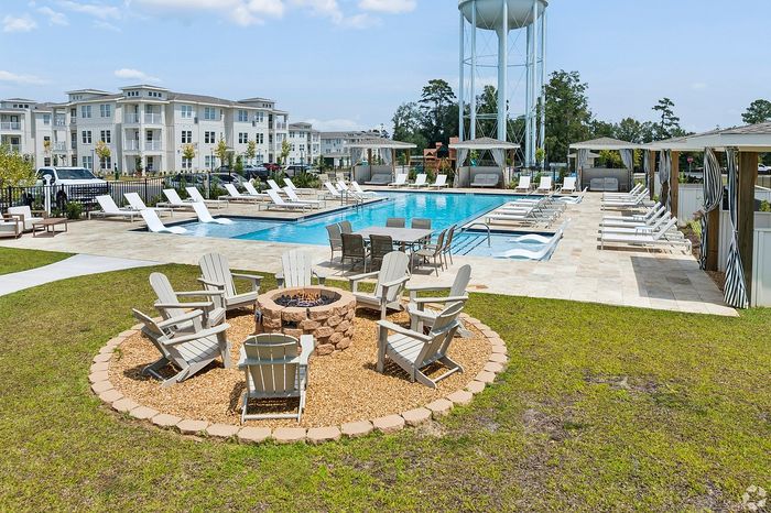 Luxurious apartment community featuring a pristine swimming pool, stylish cabanas, and an inviting fire pit area surrounded by comfortable seating.