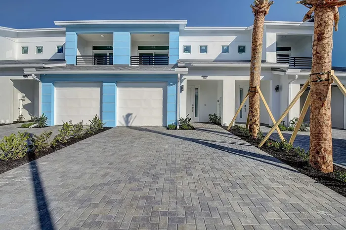 Modern duplex with sleek design, featuring vibrant blue accents and elegant palm trees in a sunny setting.