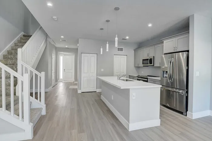 Modern open-concept kitchen with stainless steel appliances, elegant pendant lighting, and sleek hardwood floors, adjacent to a stylish staircase.