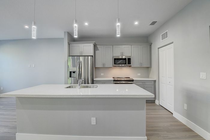 Contemporary kitchen with sleek gray cabinets, stainless steel appliances, and a sparkling quartz island featuring modern pendant lighting.