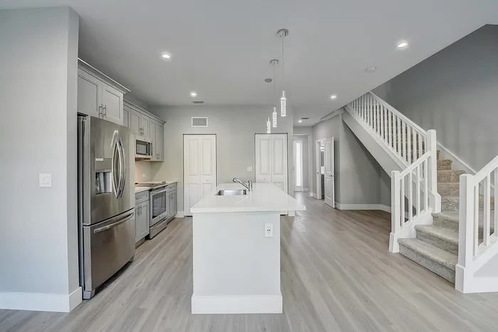 Modern kitchen design featuring sleek stainless steel appliances, elegant lighting, and a spacious island with quartz countertop, complemented by a stylish staircase.