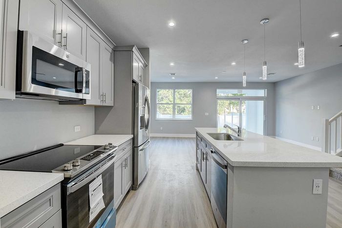 Modern kitchen with sleek stainless steel appliances, quartz countertops, and elegant pendant lighting leading into a bright, open-concept living space.