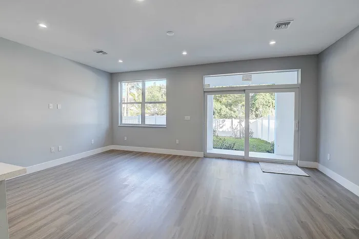 Bright living space with modern wood flooring, large windows, and sliding glass doors opening to a lush backyard.