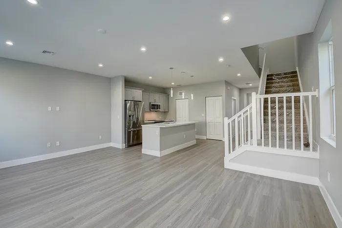 Modern open-concept living space with sleek kitchen, stainless steel appliances, and elegant staircase.
