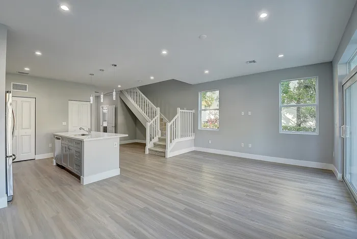 Bright open-plan living area with modern kitchen island, sleek wooden flooring, and elegant staircase leading to upper floor.