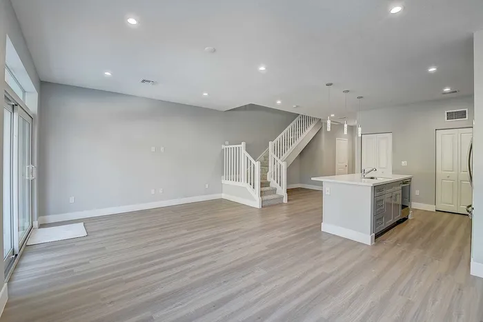 Modern open-concept living area with sleek flooring, elegant staircase, and a stylish kitchen island, perfect for entertaining.
