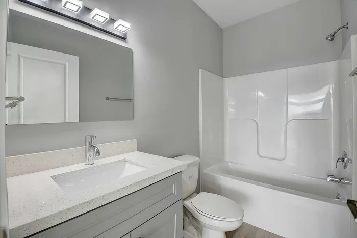 Modern bathroom showcasing a sleek vanity with a polished countertop, elegant mirror, and a stylish bathtub surrounded by soft gray walls.