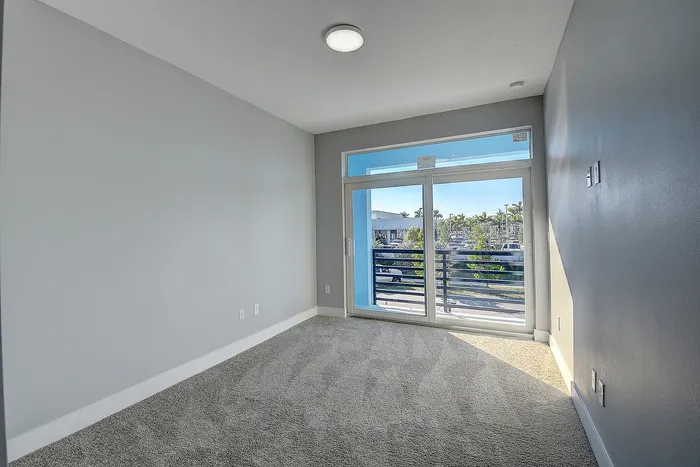 Bright and inviting bedroom featuring plush carpet, soft gray walls, and large sliding doors leading to a private balcony with serene views.