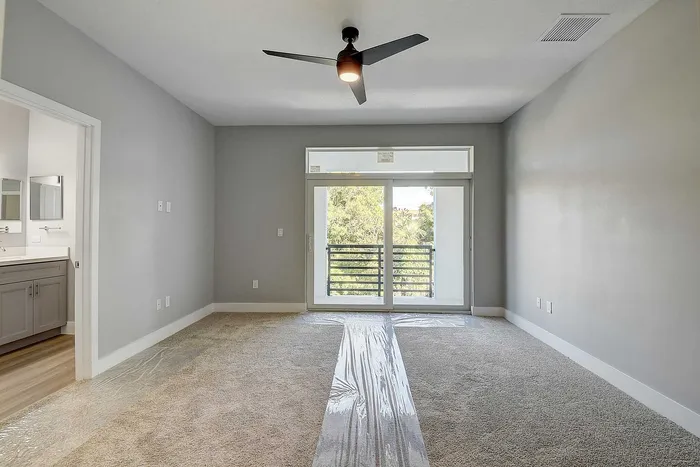 Bright and airy bedroom with modern ceiling fan, plush carpeting, and sliding glass doors leading to a serene balcony view.