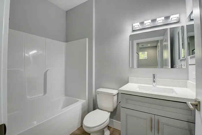 Modern bathroom with elegant lighting, sleek vanity, and spacious bathtub, complemented by soft gray tones for a relaxing ambiance.
