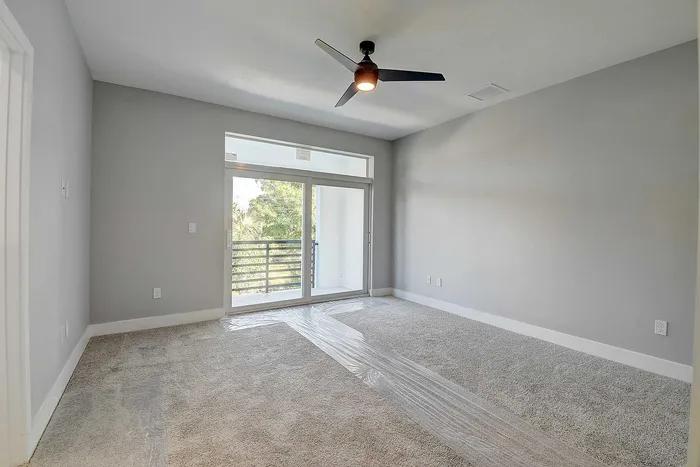 Bright and airy bedroom with plush carpets, modern ceiling fan, and large glass doors leading to a private balcony with lush views.
