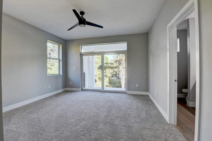 Bright and airy bedroom featuring plush carpet, modern ceiling fan, and large sliding glass doors opening to a serene view.