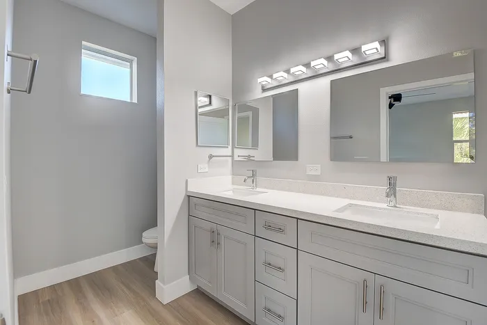 Luxurious bathroom featuring elegant double vanities, pristine mirrors, and modern lighting with sleek gray cabinetry.