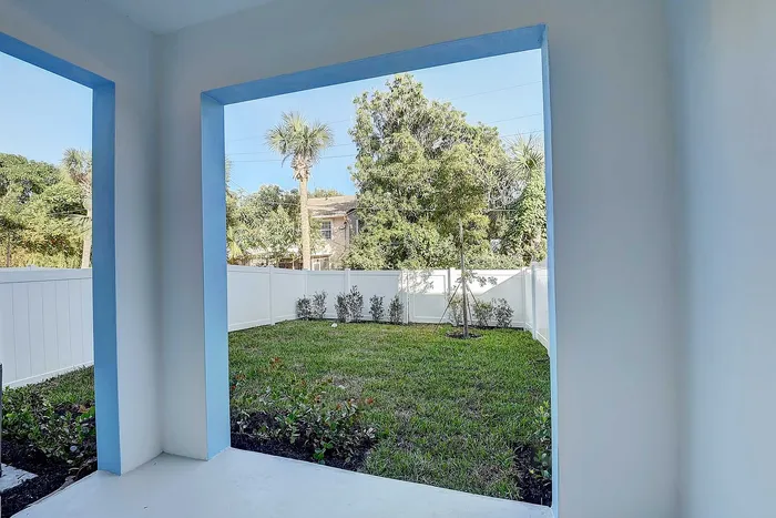 Charming view from a cozy patio overlooking a lush green backyard with tropical palm trees and a privacy fence.
