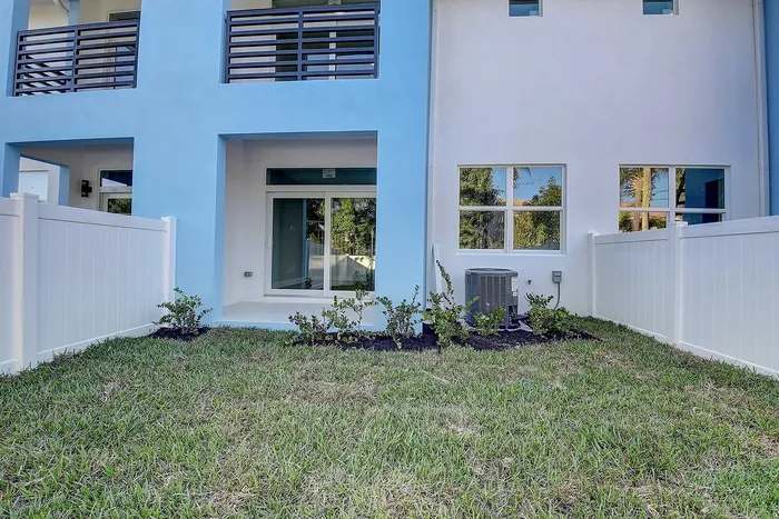 Bright view of a beautiful modern apartment exterior with blue and white design, private fenced yard, and lush green lawn.