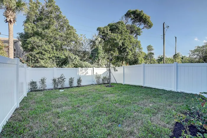Charming backyard with lush green grass, bordered by a modern white fence and surrounded by vibrant trees, perfect for outdoor relaxation.