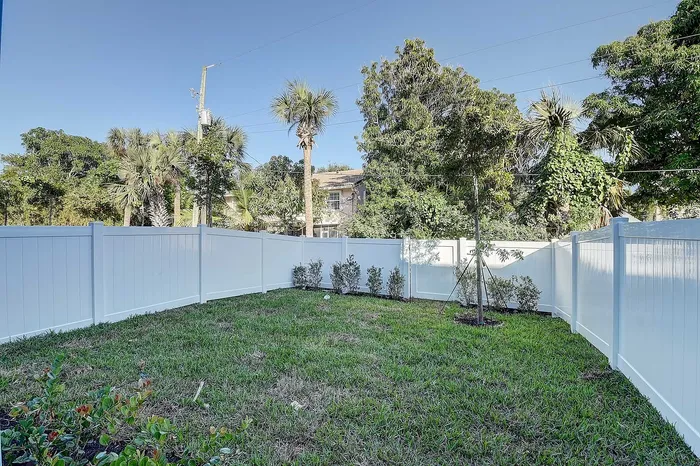 Private backyard oasis with lush greenery, white fenced perimeter, and vibrant garden touches, offering serene outdoor living.