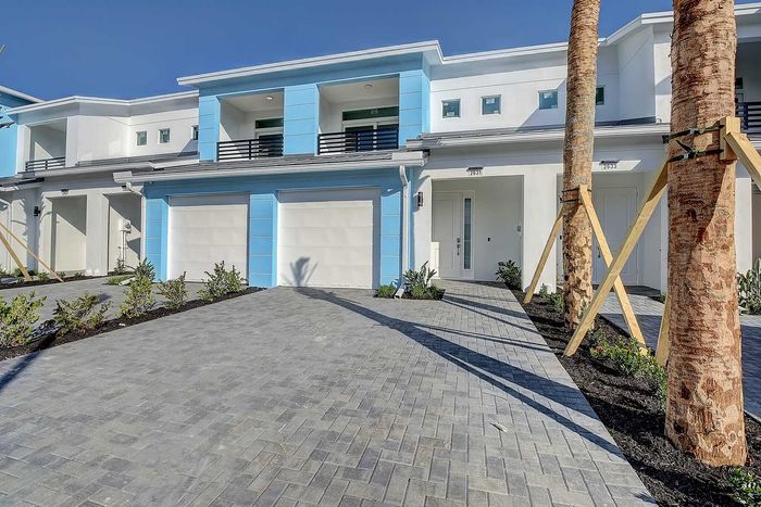 Modern townhouse facade with vibrant blue accents, featuring spacious driveways and lush landscaping under clear blue skies.
