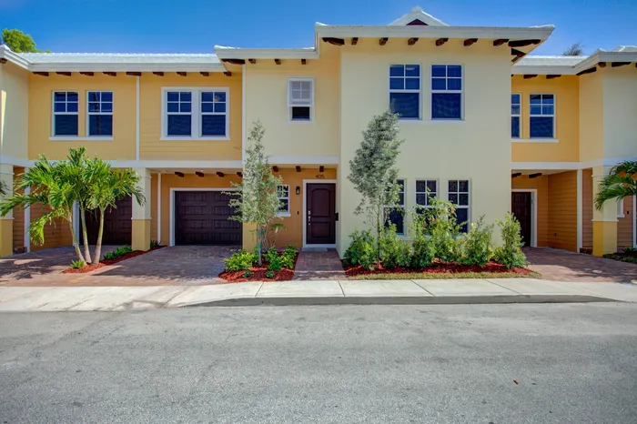 Charming two-story townhouse exterior with vibrant yellow facade, lush landscaping, and a double car garage, perfect for modern living.