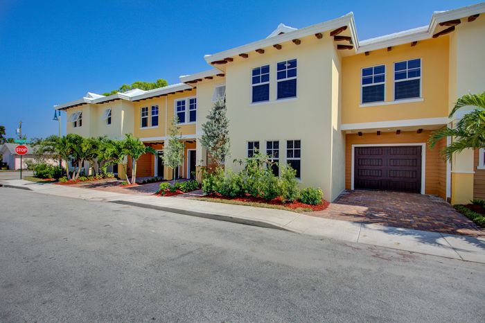 Charming townhouse exterior with vibrant yellow facade, lush landscaping, and elegant architecture under a bright blue sky.