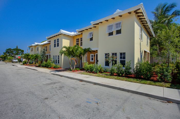 Charming yellow apartment complex with lush landscaping and palm trees under a bright blue sky.